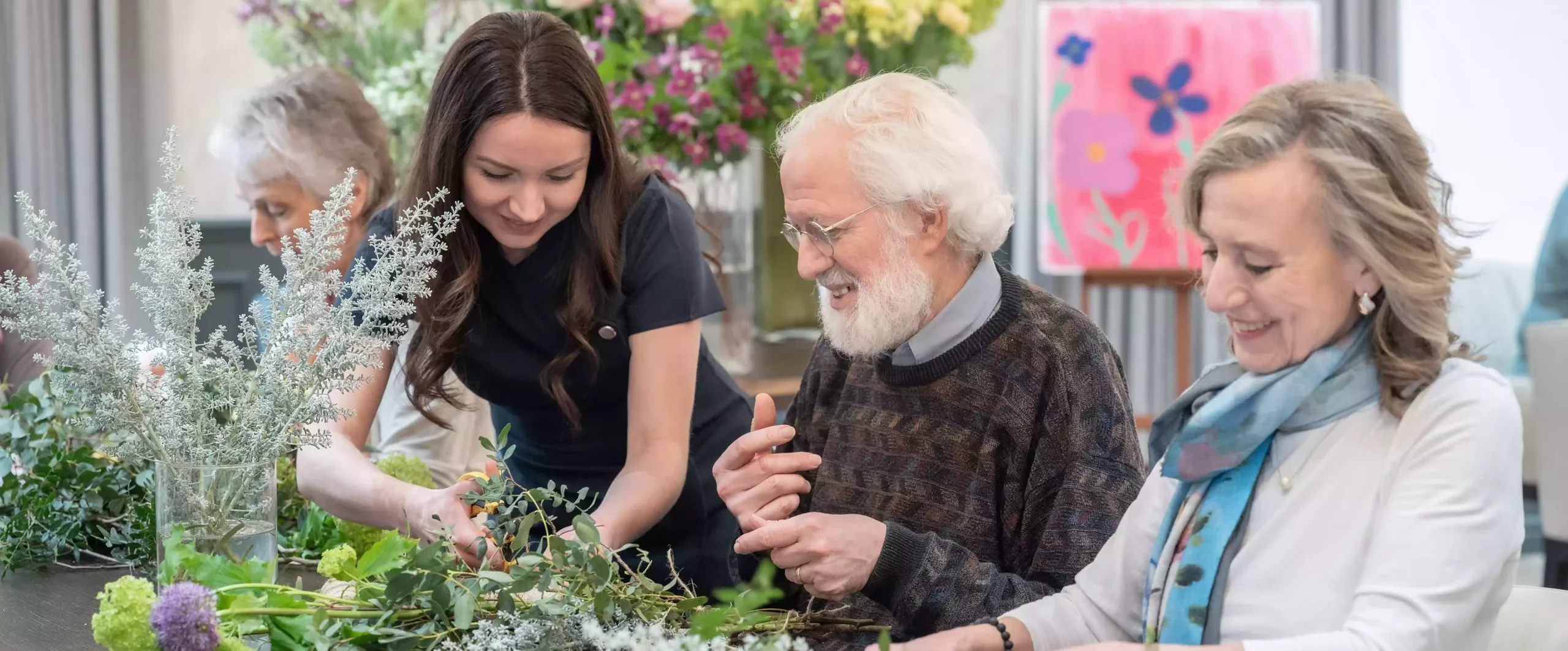 Elderly residents enjoying a flower arranging activity with a care professional in a luxury care home.